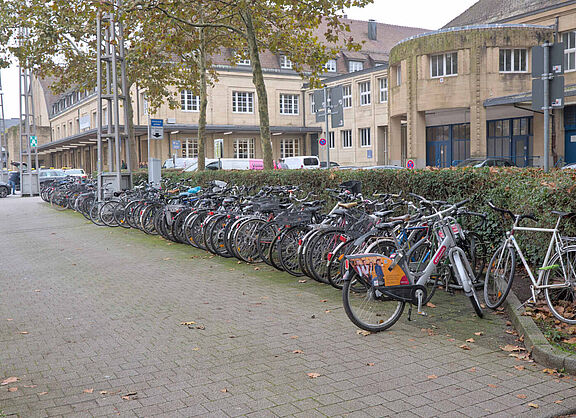 Blick auf einen komplett gefüllten Fahrradständer, im Hintergrund ist der Taxistand und das Bahnhofsgebäude zu sehen