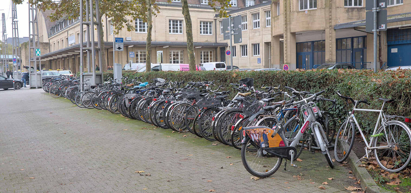 Blick auf einen komplett gefüllten Fahrradständer, im Hintergrund ist der Taxistand und das Bahnhofsgebäude zu sehen