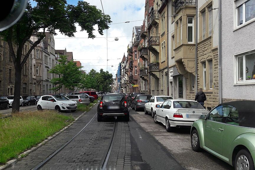 Ansicht der westlichen Kriegsstraße - hier muss ein Radweg hin Kriegsstraße aus Sicht eines Fahrzeugs, rechter Straßenrand mit parkenden Fahrzeugen belegt, PKW auf der Fahrbahn, linker Bildrand zeigt den Grünstreifen in der Straßenmitte.