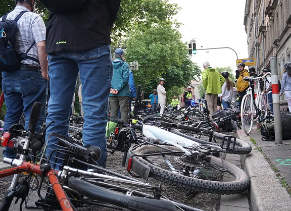 In der Kapellenstraße legen Radfahrende ihre Fahrräder am Unfallort nieder. Blick aus Kniehöhe vom Bordstein aus. Am Bordstein steht das Ghostbike.