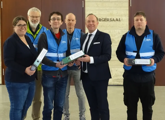 Das Foto zeigt mehrere Personen, die Herrn Bürgermeister Daniel Fluhrer drei Aktenordner übergeben und dabei in die Kamera schauen.